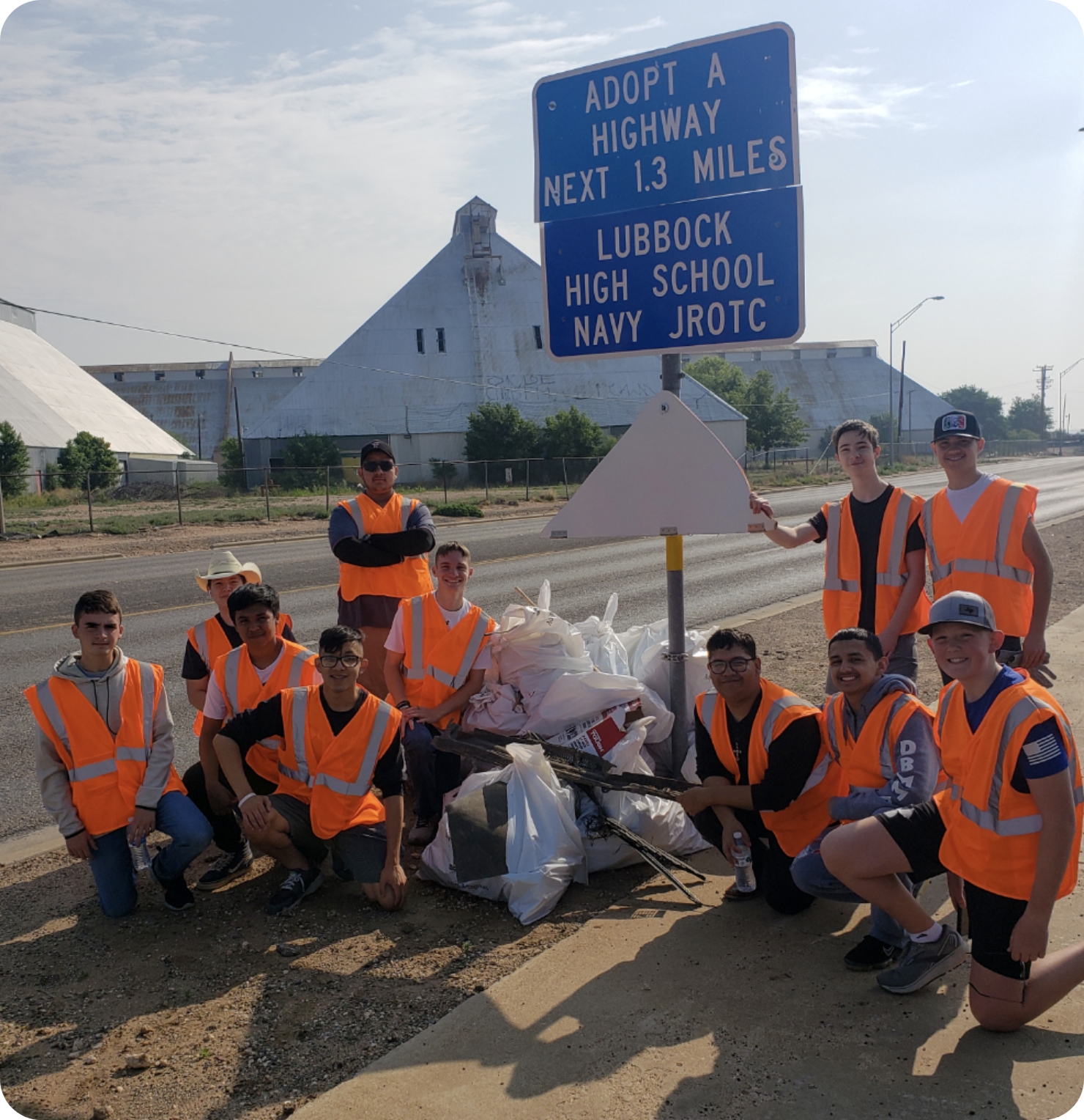 "Lubbock High School Navy JROTC" volunteers pose in front of the trash bags they have picked up on a highway.